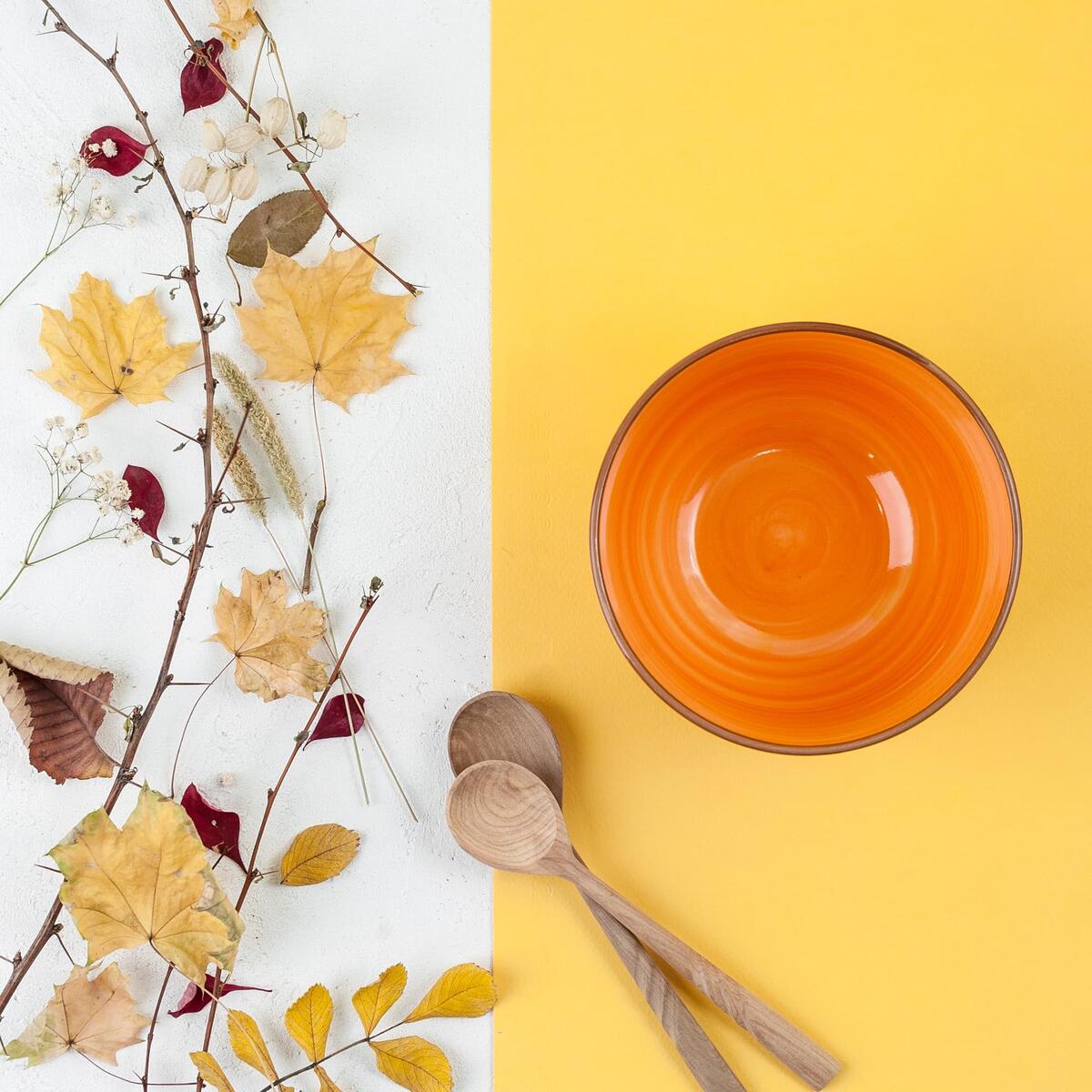 Bright Orange Empty Bowl Wooden Spoon And Autumn Leaves On A Ye